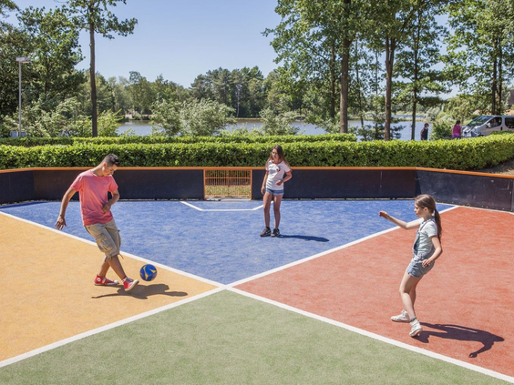 Gezin speelt een balspel in de kleurrijke pannakooi of het multi-court op Camping de Schatberg.