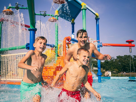 Vrolijke kinderen rennen en spelen tussen de fonteinen en sproeiers in de outdoor waterspeeltuin op Camping de Schatberg.