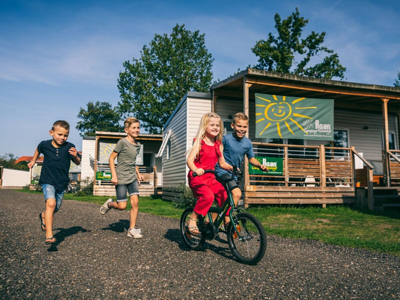 Kinderen rennen, fietsen en spelen samen op de paden bij de stacaravans van Camping de Schatberg.