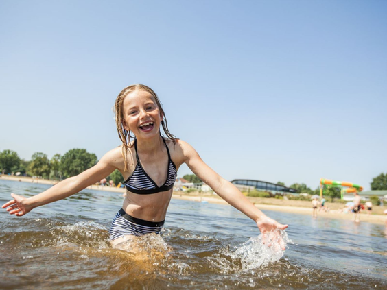 Meisje speelt en spettert vrolijk in het water van het recreatiemeer op Camping de Schatberg.