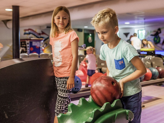 Twee kinderen, een jongen en een meisje, zijn aan het bowlen op de bowlingbaan van Camping de Schatberg.