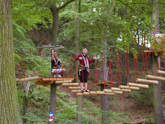 Een meisje balanceert behendig over een touwbrug hoog tussen de bomen in het klimbos Kletterwald Eschwege.