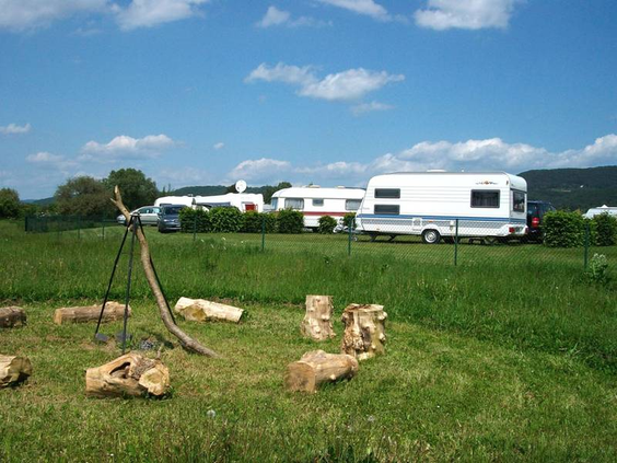 Ruime, groene kampeerplaats op Knaus Campingpark Eschwege met een kampvuurkring van houten stammen op de voorgrond.