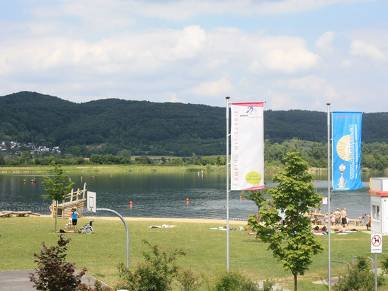 Uitzicht op de Werratalsee vanaf de ligweide van Knaus Campingpark Eschwege, waar mensen zonnen en zwemmen.