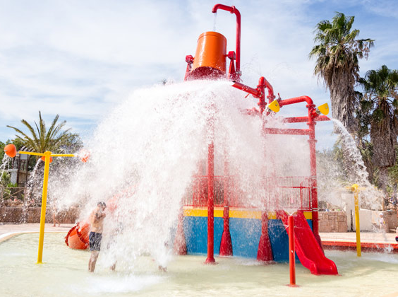 Een grote emmer stort water uit over een speelplaats in een buitenzwembad