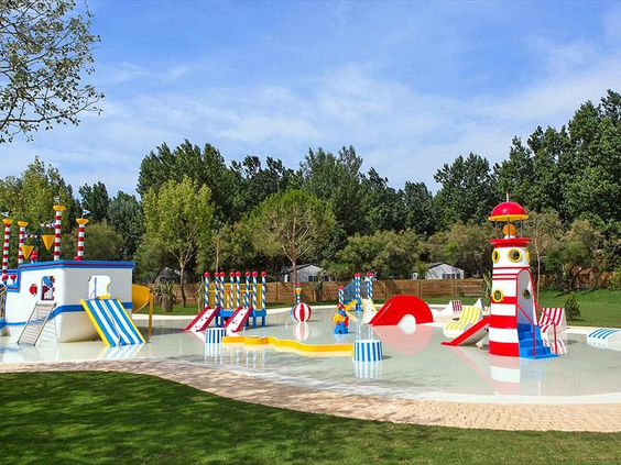 Overzicht van de kleurrijke waterspeeltuin voor peuters en kleuters met glijbanen en een vuurtoren op Camping Le Sérignan Plage.