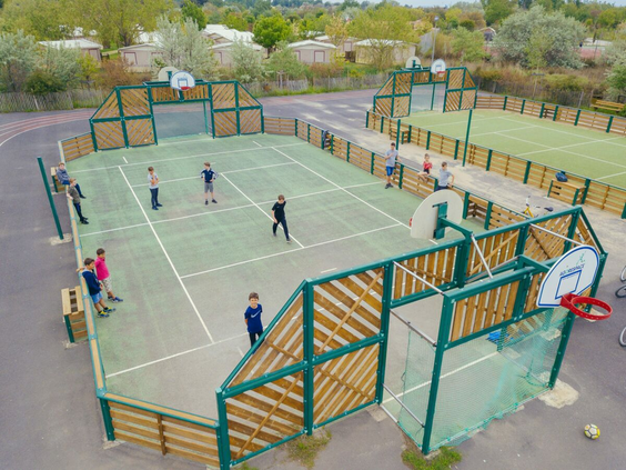 Kinderen voetballen en spelen op het omheinde multisportterrein met goals en baskets op Camping Le Sérignan Plage, gezien van bovenaf.
