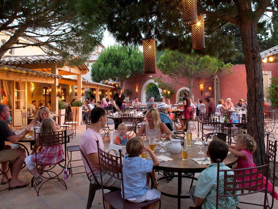 Gezinnen dineren op het sfeervol verlichte terras van het restaurant op Camping Le Sérignan Plage tijdens een warme zomeravond.