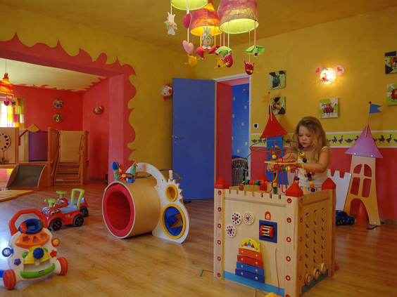 Kleurrijke binnenspeelruimte voor baby's en peuters, met veilig, houten speelgoed en een meisje dat speelt bij een speelkasteel.