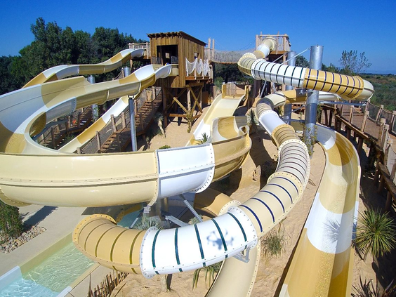 Overzicht van de vele kronkelende, geel-witte waterglijbanen en buizen in het grote aquapark van Camping Le Sérignan Plage.