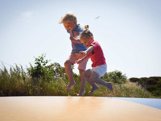 Twee kinderen springen hoog in de lucht op de airtrampoline in de duinen van Camping Loodsmansduin.