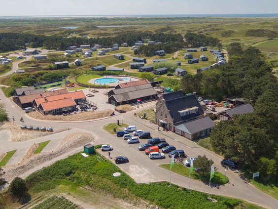 Een luchtfoto van Camping Loodsmansduin met het centrumgebouw en het buitenzwembad, gelegen in het duinlandschap van Texel.