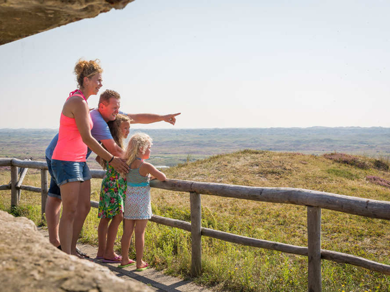 Een gezin met twee kinderen kijkt vanaf een uitkijkpunt met een houten hek uit over het uitgestrekte duinlandschap van Texel.