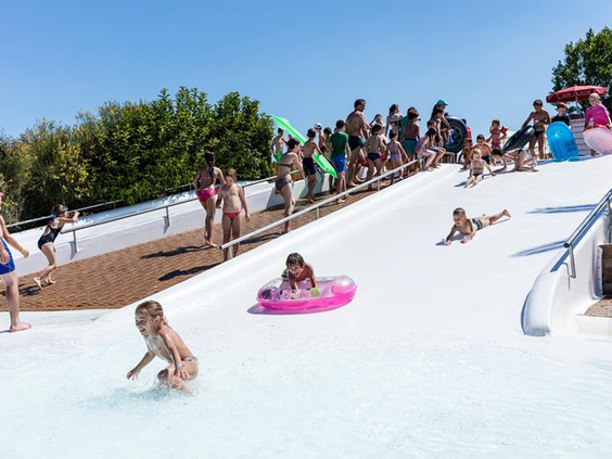 Kinderen glijden met en zonder zwembanden van de brede, zachte glijheuvel in het lagune zwembad van de kindvriendelijke camping Park Albatros.