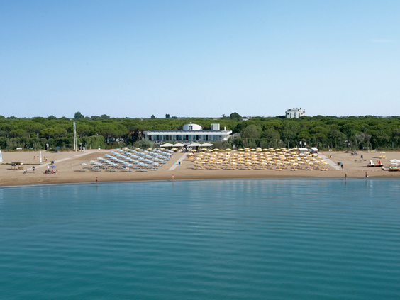 Het privéstrand van Camping Union Lido gezien vanaf de zee, met vele rijen geordende ligbedjes en parasols en een strandpaviljoen.