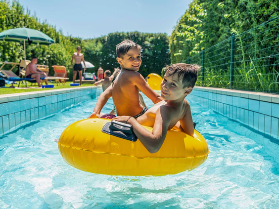 Twee lachende jongens dobberen samen in een grote gele opblaasband in de lazy river van Camping Union Lido op een zonnige dag.