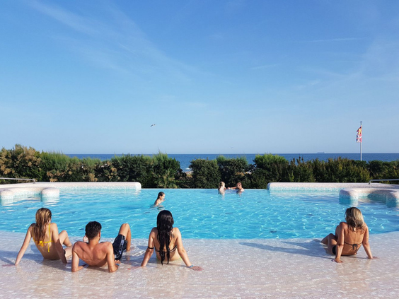 Jongeren en volwassenen ontspannen aan de rand van het zwembad op Camping Union Lido, met een prachtig uitzicht over het strand en de zee.