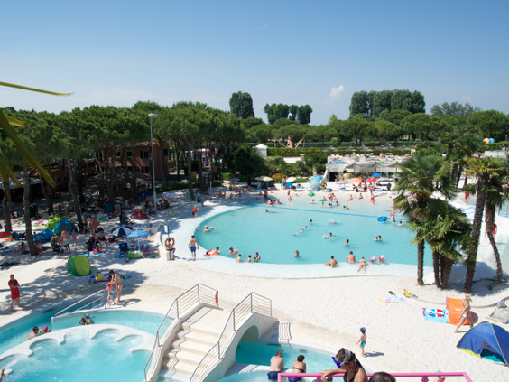 Vakantiegangers genieten van het zwembad met een witte loopbrug en omringd door palmbomen op Camping Union Lido in Italië.