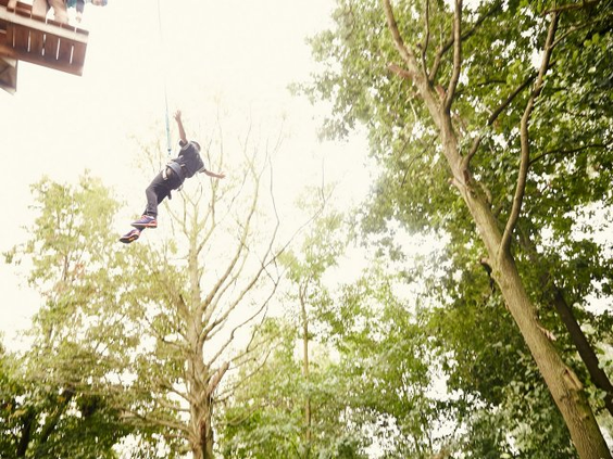 Iemand zoeft hoog tussen de bomen via de zipline van het klimparcours High Adventure Experience bij Center Parcs Bispinger Heide.