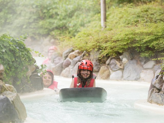 Een meisje met helm en zwemvest glijdt op een bodyboard over het water in het buitenbad van de Aqua Mundo bij Center Parcs Bispinger Heide.