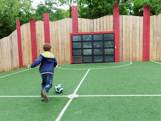 Een jongen schiet een voetbal richting het doel in de omheinde voetbalkooi (Soccer Cage) op kunstgras bij Center Parcs Bispinger Heide.
