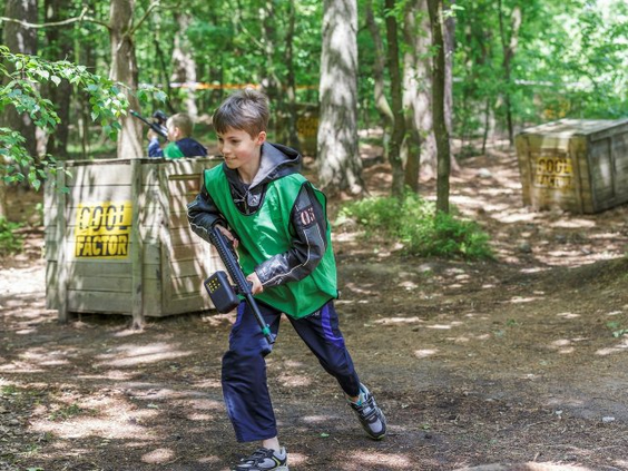 Een jongen met een groen hesje en een lasergun rent door het bos tijdens een potje Outdoor Laser Battle bij Center Parcs Bispinger Heide.
