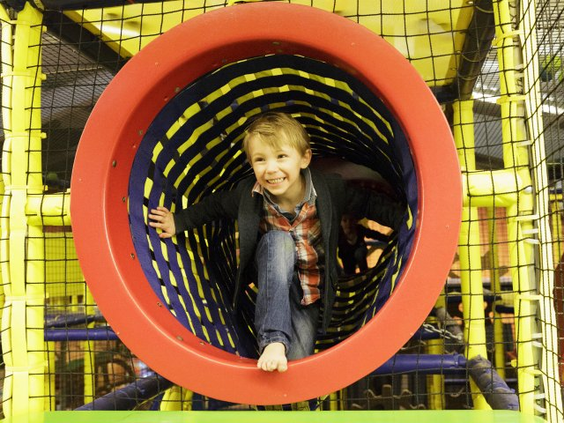 Een lachende jongen kruipt door een ronde, rode tunnel in het grote klim- en klauterparadijs van de BALUBA binnenspeeltuin.