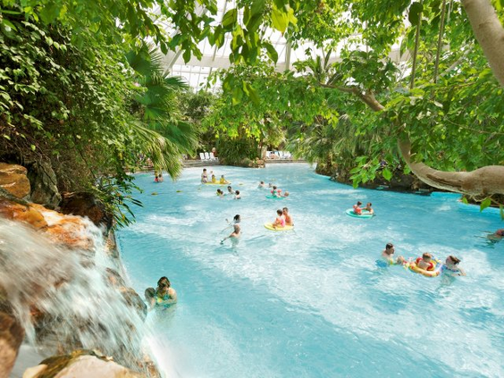 Bezoekers laten zich op zwembanden meevoeren door de stroming van de wildwaterbaan, omringd door tropische planten in de Aqua Mundo van Center Parcs Bispinger Heide.