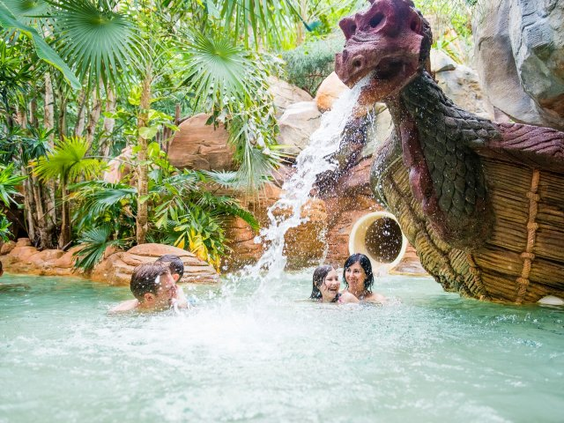 Een gezin speelt vrolijk in het water onder een grote draak die water spuwt in het kinderbad van de Aqua Mundo in Center Parcs Bispinger Heide.