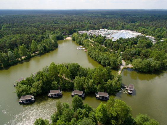 Luchtfoto van Center Parcs Bispinger Heide, met de unieke woonboten op het meer, omringd door het groene bos van de Lüneburger Heide.