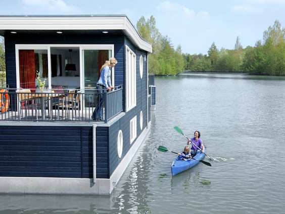 Een familie in een kajak vaart op het meer langs een van de moderne woonboten van Center Parcs Bispinger Heide.