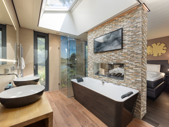 Een luxe wellness badkamer in een Eden cottage bij Center Parcs De Kempervennen, met een vrijstaand bad, een regendouche en uitzicht naar buiten.