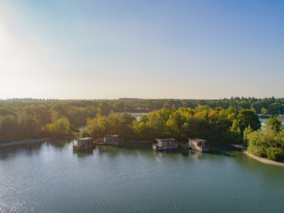 Een luchtfoto van Center Parcs De Kempervennen, met een prachtig uitzicht over het meer, de woonboten en de omliggende groene bossen.