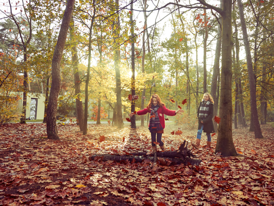 Twee kinderen gooien vrolijk met herfstbladeren in het bos bij Center Parcs De Kempervennen tijdens een zonnige herfstdag.
