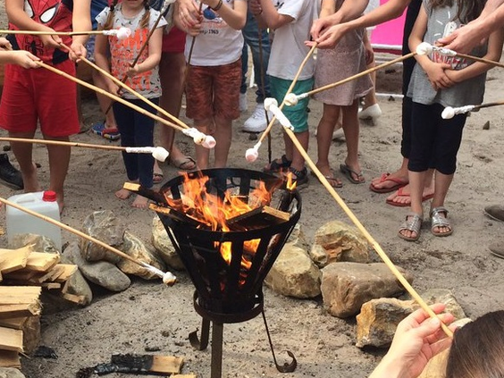 Een groep kinderen roostert marshmallows op lange stokken boven een vuurkorf tijdens een activiteit bij Center Parcs De Kempervennen.