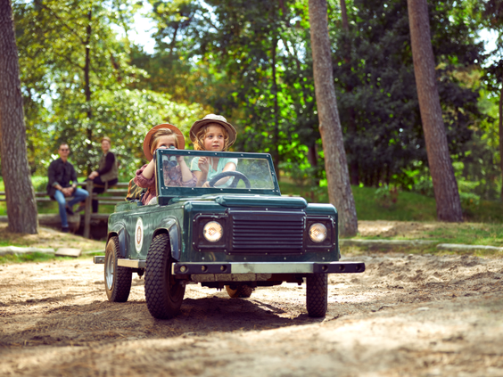 Twee kinderen rijden in een groene speelgoed-jeep over een bospad tijdens de Kids Safari bij Center Parcs De Kempervennen.