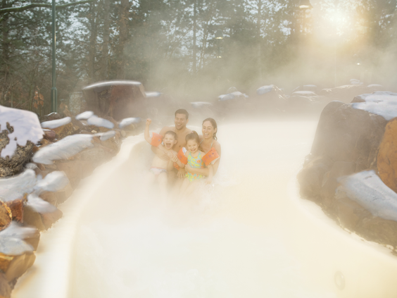 Een gezin geniet van het warme, stomende water in het buitenbad van de Aqua Mundo bij Center Parcs De Kempervennen, omringd door een besneeuwd landschap.