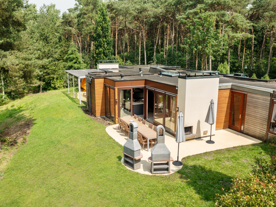 De buitenkant van een luxe en moderne Eden cottage bij Center Parcs De Kempervennen, gelegen in het bos met een grote tuin en een terras.