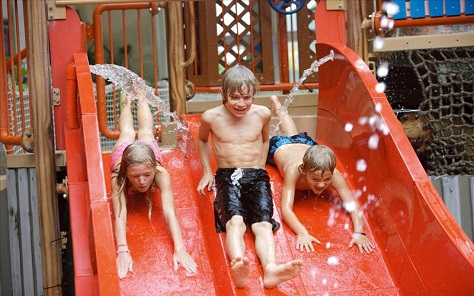 Drie kinderen glijden tegelijk van de brede, rode familieglijbaan in het Aqua Mundo zwembad van Park Hochsauerland.