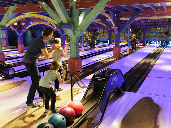 Een gezin is aan het bowlen op de kleurrijk verlichte bowlingbanen in de Market Dome van Center Parcs Het Meerdal.