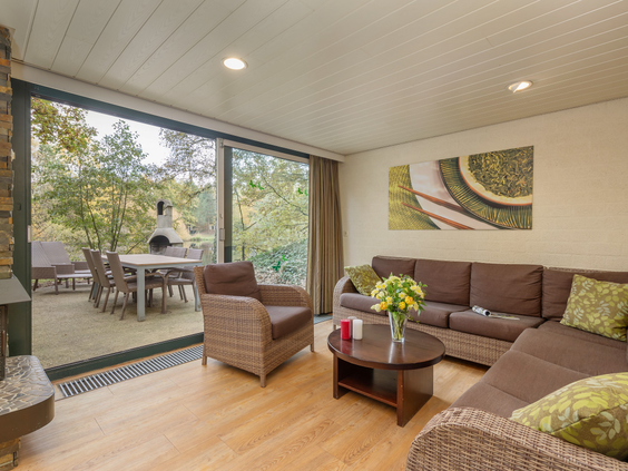 De gezellige woonkamer van een cottage in Het Meerdal met een comfortabele hoekbank en een grote glazen schuifpui die uitzicht biedt op het privéterras