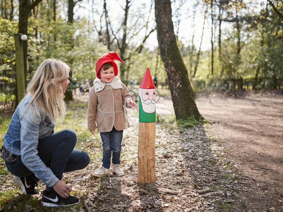 Een moeder en haar kind met een kaboutermuts op staan bij een kabouterpaaltje op het Kabouterpad in de bossen van Center Parcs Het Meerdal.