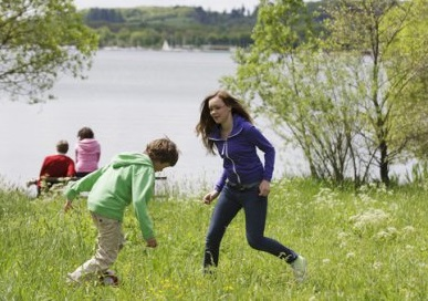 Kinderen spelen en rennen vrolijk in het gras aan de oever van het grote Bostalmeer bij Center Parcs.