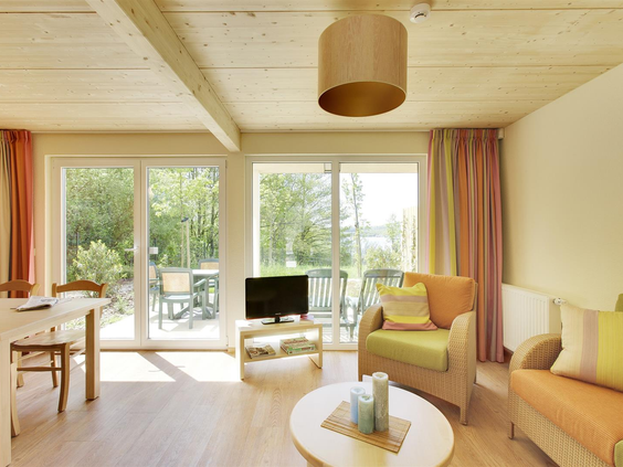 De lichte en moderne woonkamer van een cottage bij Center Parcs Park Bostalsee, met grote ramen die uitzicht bieden op het terras.
