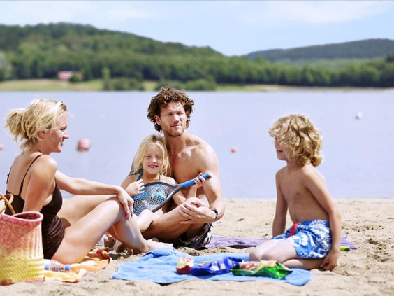 Een gezin met twee kinderen bouwt zandkastelen en speelt op het zandstrand van het Bostalmeer bij Center Parcs.