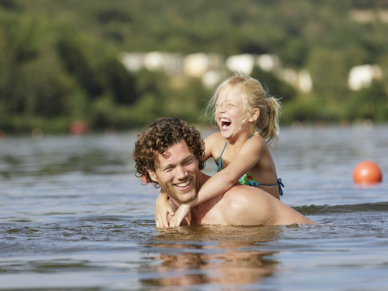 Een vader en zijn jonge dochter spelen en lachen samen in het water van het Bostalmeer.