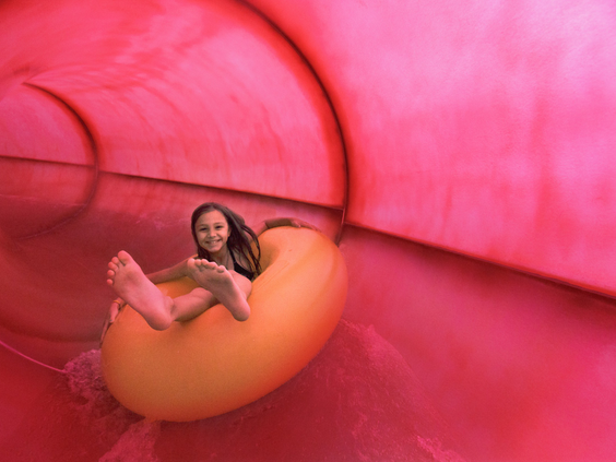 Een meisje glijdt met een lach op haar gezicht in een opblaasband door een grote, roze waterglijbaan in de Aqua Mundo.