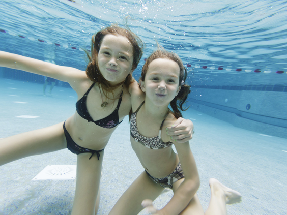 Twee meisjes poseren lachend voor de camera onder water in het heldere zwembad van de Aqua Mundo.