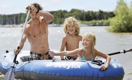 Een lachende vader met zijn twee kinderen in een opblaasbare boot op het zonnige Bostalmeer.