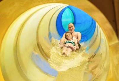 Een vader en zijn dochter glijden samen lachend door een grote gele waterglijbaan in het subtropische zwemparadijs Aqua Mundo.